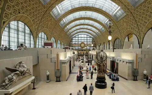 Une salle de musée spacieuse avec un plafond en verre voûté, des sculptures et des visiteurs marchant et s'asseyant sur des bancs.