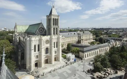 Historische Basilique Cathédrale de Saint-Denis met groen dak en hoge toren, omgeven door bomen op een zonnige dag.