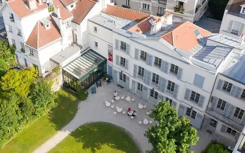Vue aérienne d'une cour avec plusieurs tables et chaises, entourée de bâtiments blancs aux toits rouges et d'un espace vitré.