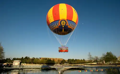 Kleurrijke Ballonvluchten Parijs boven een vijver en aanlegsteiger, omringd door bomen onder een blauwe lucht.
