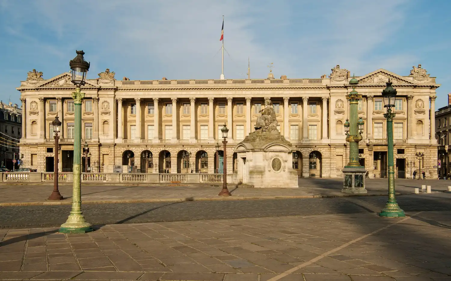 Zabytkowy Hôtel de la Marine z francuską flagą, zdobną fasadą, kolumnami i posągiem na kamiennym placu.