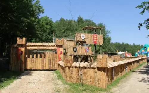 Houten kasteel met torens en vlaggen in een bos onder een helderblauwe lucht bij Sherwood Parc.