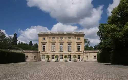 Het landgoed van Marie-Antoinette: klassiek beige gebouw met hoge ramen en bomen bij een binnenplaats van kasseien.