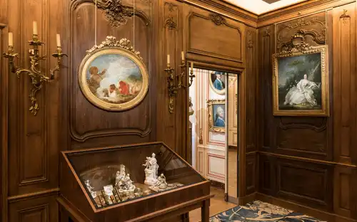 Elegancki osiemnastowieczny salon w Musée Cognacq-Jay Musée Cognacq-Jay: ozdobny pokój z boazerią, złotymi kinkietami, obrazami i gablotą z porcelanowymi figurkami.
