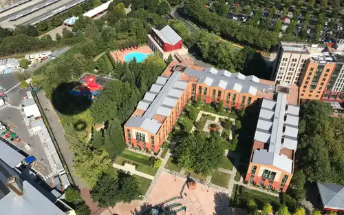 Luchtfoto van PanoraMagique met oranje gebouwen, groene binnenplaatsen, speeltuin, zwembad en parkeerplaats.