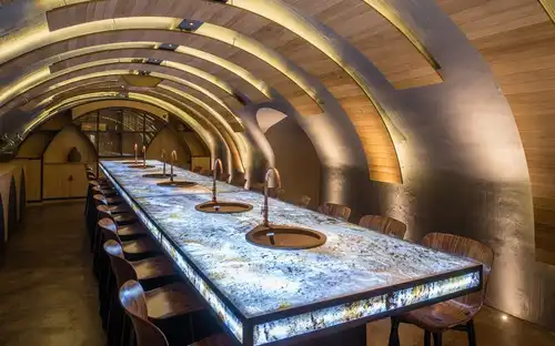 Moderne bar bij Les Caves du Louvre met een gewelfd houten plafond, marmeren bar en warme geïntegreerde verlichting.