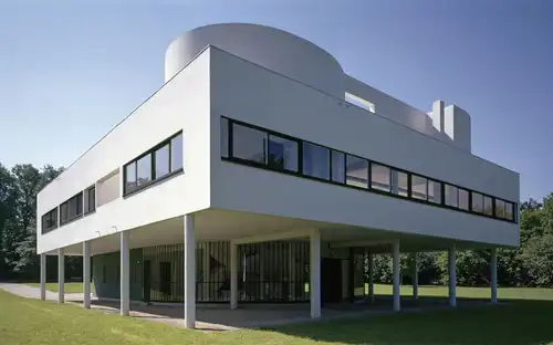 Modern wit minimalistisch gebouw Villa Savoye op palen met lange ramen op een grasveld met bomen onder een heldere lucht.
