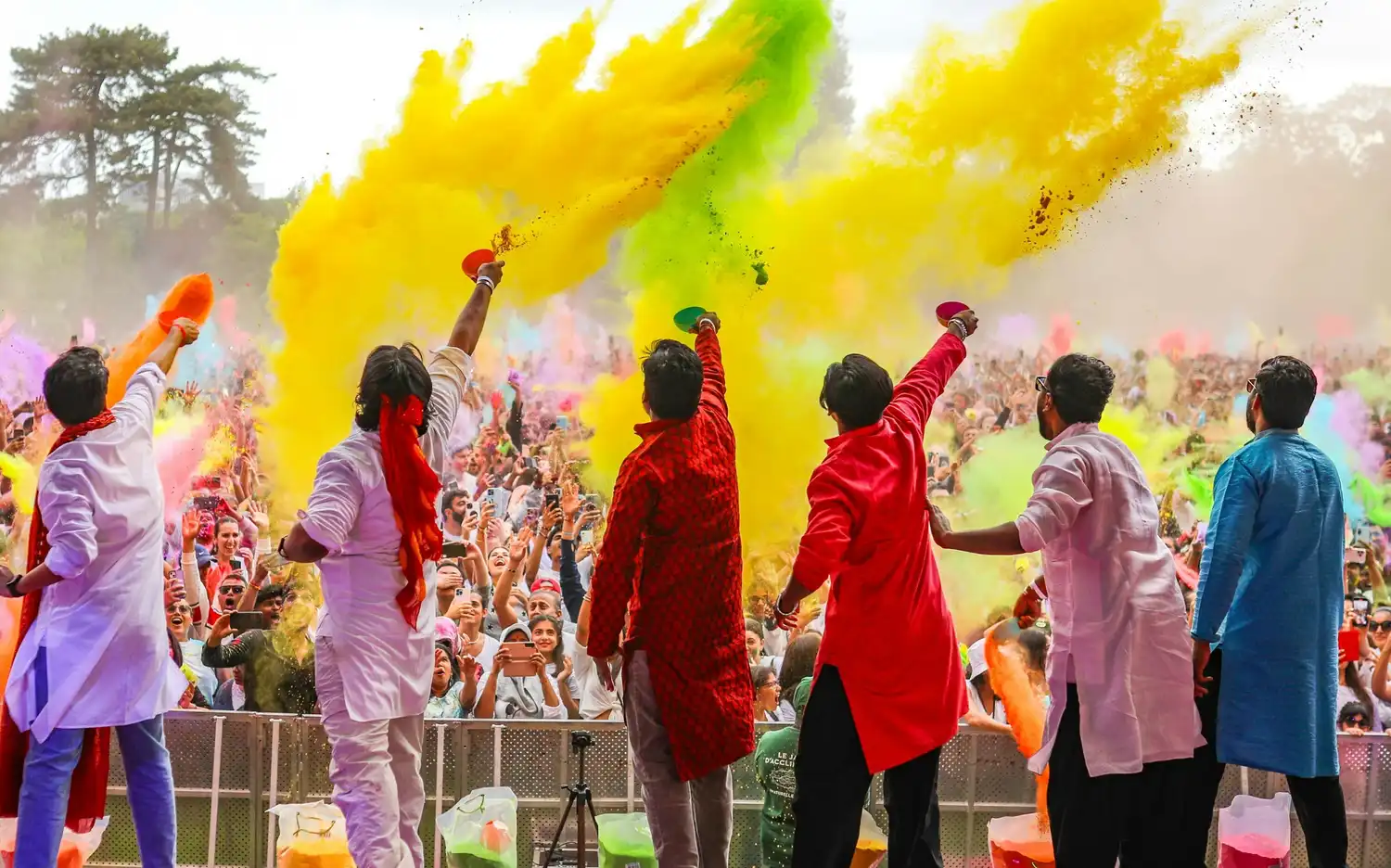 Crowd at Jardin d'Acclimatation celebrating Holi with a vibrant explosion of colorful powders in the Parisian sky.