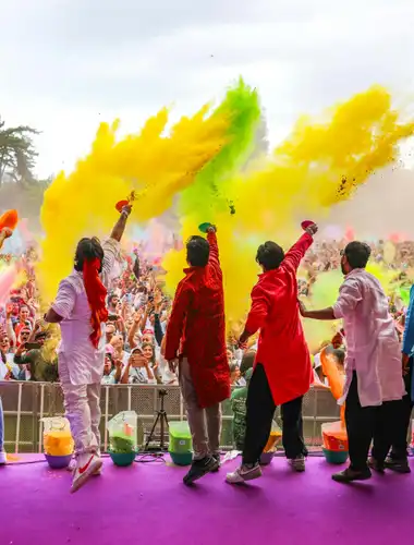 Crowd at Jardin d'Acclimatation celebrating Holi with a vibrant explosion of colorful powders in the Parisian sky.