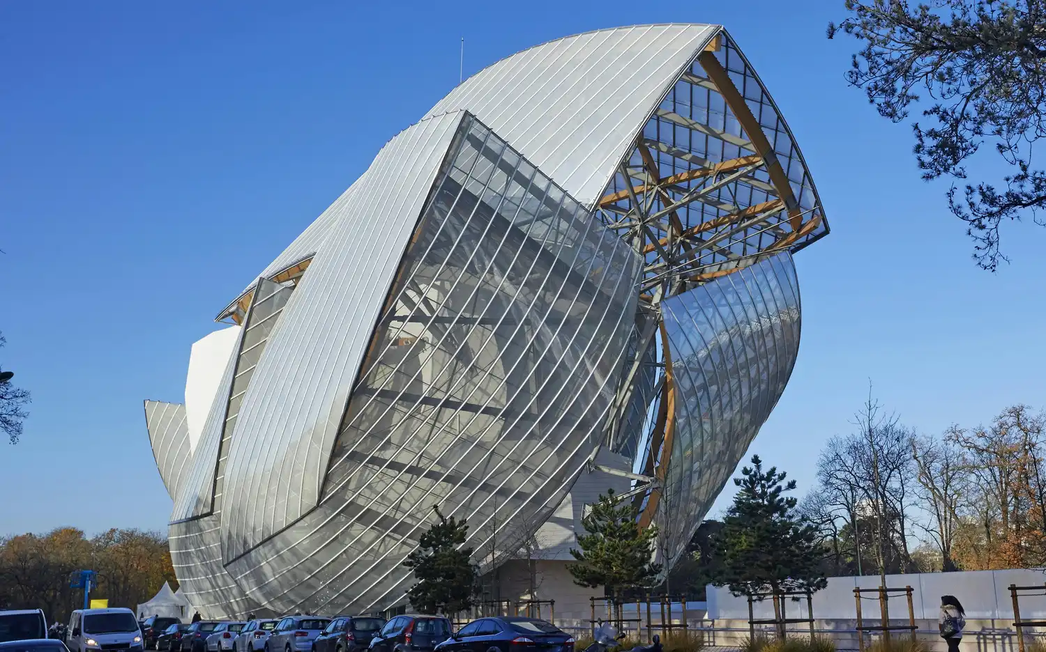 Bâtiment moderne avec un design unique de verre et de métal incurvé, voitures garées devant, arbres sur la droite et ciel bleu clair. Bâtiment moderne avec un design unique de verre et de métal incurvé, voitures garées devant, arbres sur la droite et ciel bleu clair.
