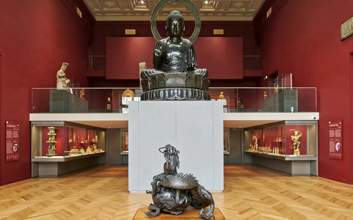 Une galerie de musée avec une grande statue de Bouddha, des vitrines d'objets et une sculpture de dragon au premier plan. Une galerie de musée avec une grande statue de Bouddha, des vitrines d'objets et une sculpture de dragon au premier plan.