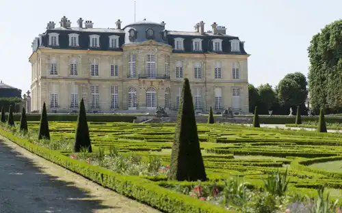 Groot historisch gebouw met verzorgde tuinen, strakke hagen en kegelvormige struiken bij Château de Champs-sur-Marne.