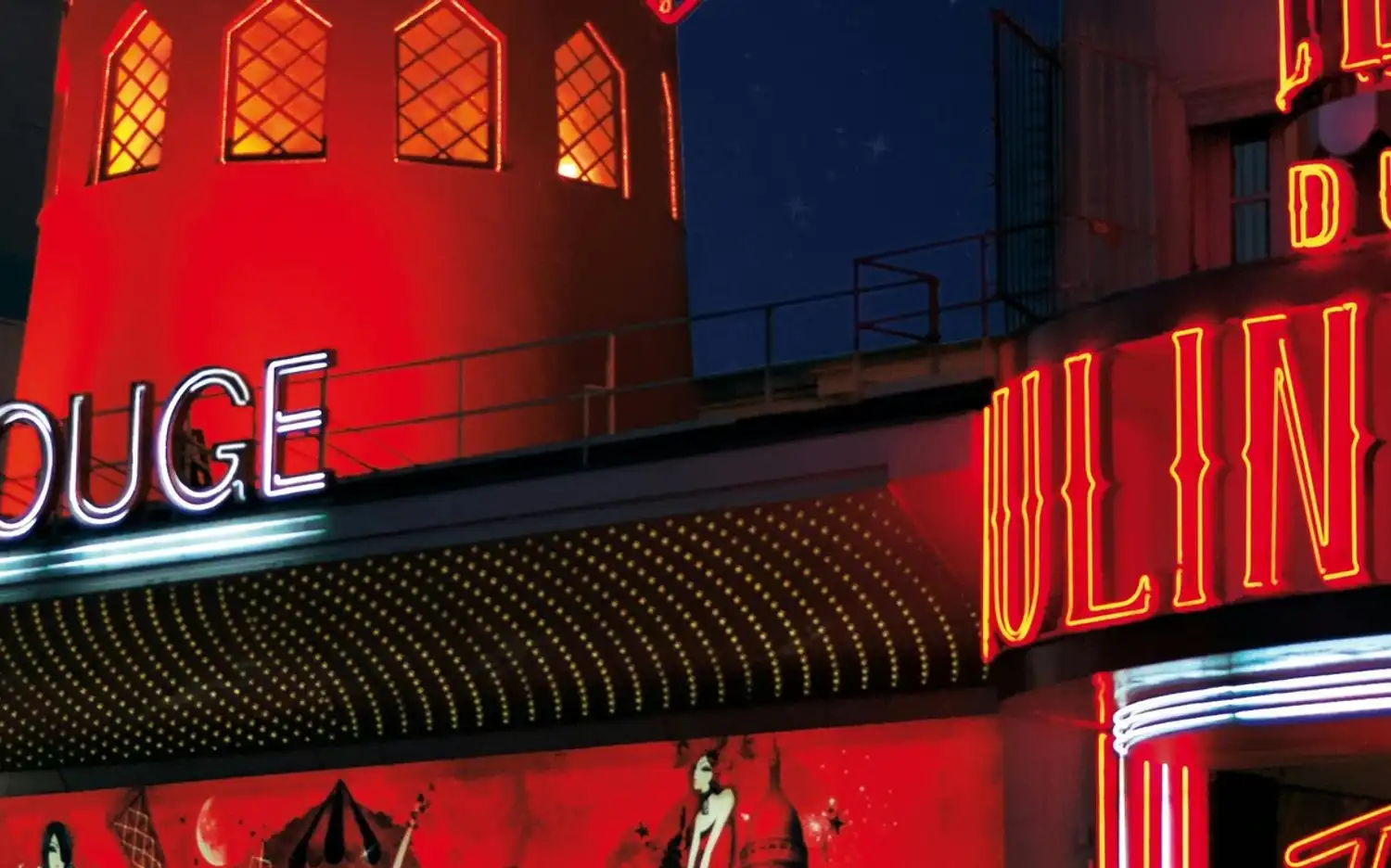 Jasne neonowe napisy Moulin Rouge nocą z oświetlonym czerwonym młynem i dekoracyjnymi światłami.