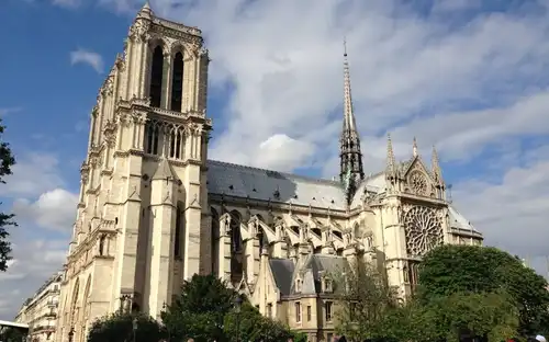 Mensenmassa voor de Kathedraal Notre-Dame in Parijs onder een lichtbewolkte hemel met zichtbare torens en spits.