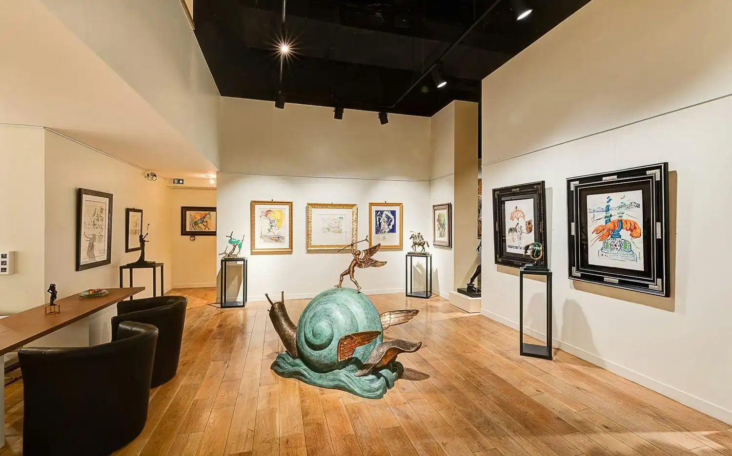Galerie d'art présentant une grande sculpture d'escargot vert avec des ailes, des œuvres d'art encadrées sur les murs et diverses sculptures sur des présentoirs.