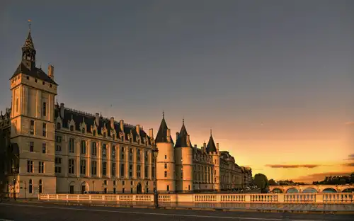 Historische Conciergerie met torens langs de Seine bij zonsondergang, met een brug onder een heldere hemel.