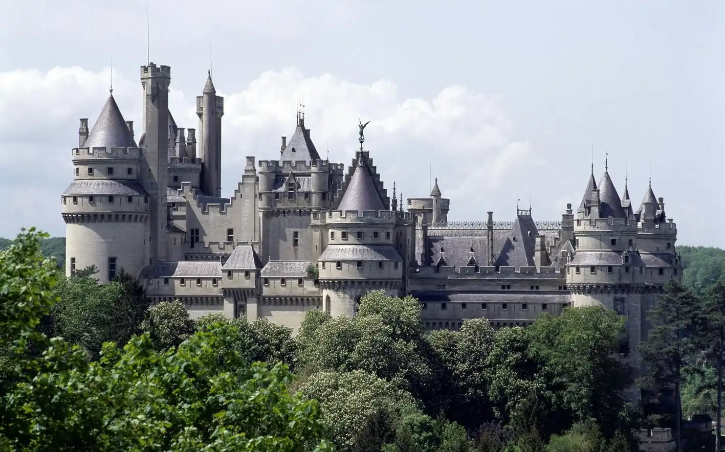 Un grand château complexe aux multiples tours et flèches, entouré d'arbres verdoyants, sur fond de ciel nuageux. Un grand château complexe aux multiples tours et flèches, entouré d'arbres verdoyants, sur fond de ciel nuageux.