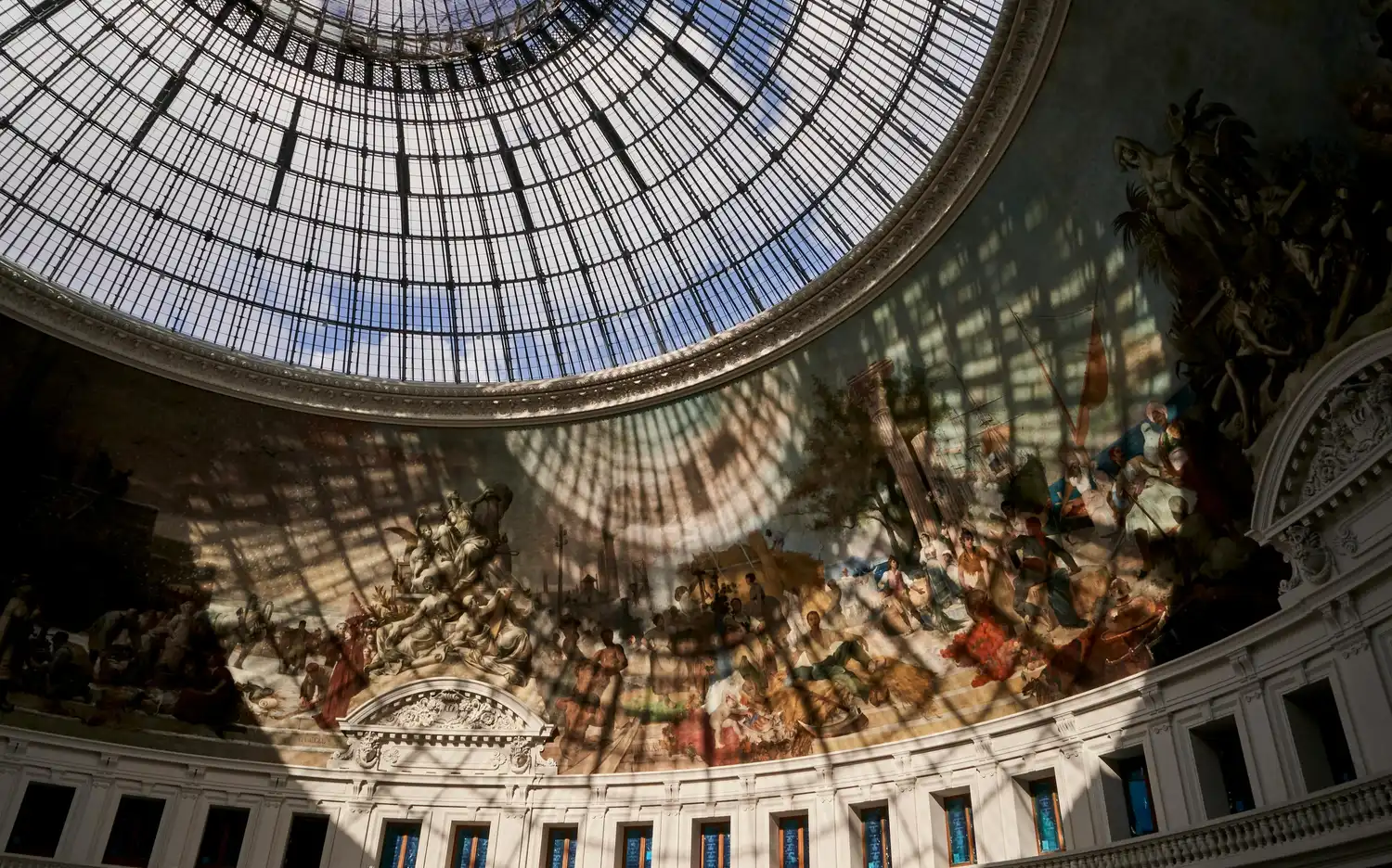Glazen koepel van Bourse de Commerce - Pinault Collection werpt schaduwen op historische en mythologische muurschilderingen.