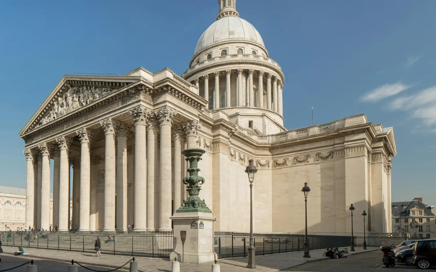Het neoklassieke Panthéon met een grote koepel en zuilen onder een blauwe lucht boven een straat met kasseien.