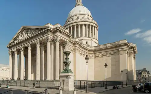 Het neoklassieke Panthéon met een grote koepel en zuilen onder een blauwe lucht boven een straat met kasseien.
